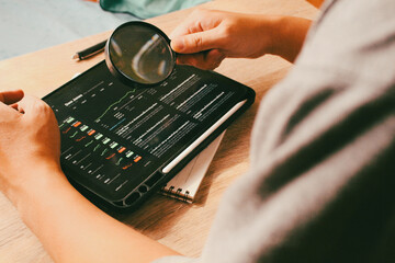 Close up of person hand holding magnifying glass to analyze stock market data on digital tablet, concept of financial research and investment inspection.