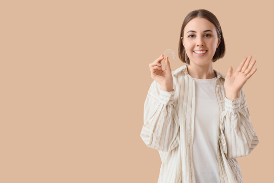 Young woman with occlusal splint showing OK on beige background