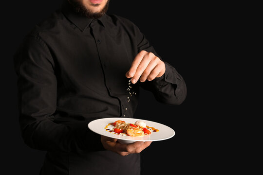 Male chef peppering tasty pasta on black background, closeup