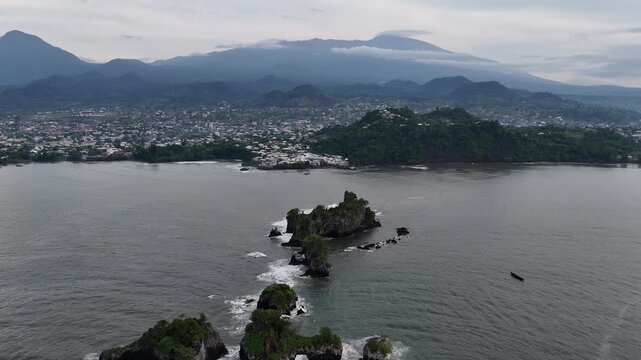 A wide-angle drone view capturing the sprawling coastal town of Limbe, Cameroon, nestled along the Atlantic Ocean and lush hills
