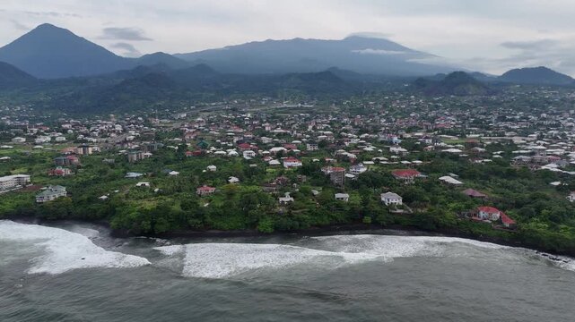 A wide-angle drone view capturing the sprawling coastal town of Limbe, Cameroon, nestled along the Atlantic Ocean and lush green hills