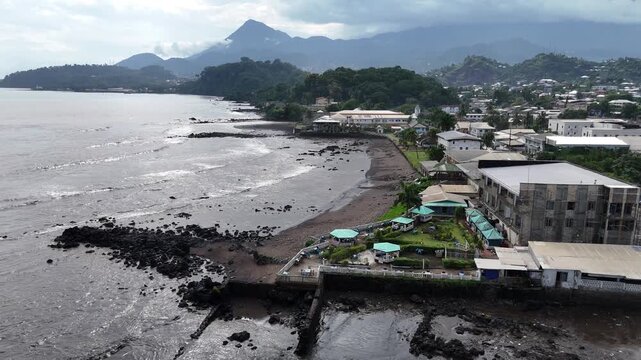 A scenic aerial vista of the Limbe shoreline, featuring the unique dark volcanic sand and residential buildings along the Atlantic coast