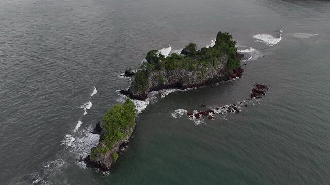 A cinematic high-angle drone perspective focusing on a lone rocky island covered in tropical vegetation in the waters near Limbe Cameroon Africa