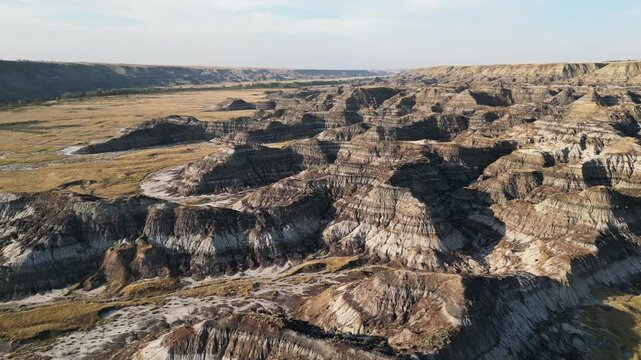 Aerial view of large eroded badlands hills in Alberta, Canada, filmed by drone shortly before sunset with warm evening light and rugged terrain visible.