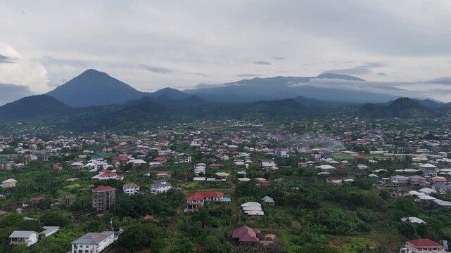A wide-angle aerial shot capturing the sprawling town of Limbe nestled against the backdrop of the majestic Mount Cameroon and its green foothills drone africa footage