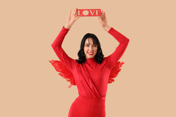 Obraz premium Beautiful young happy woman dressed as cupid with word LOVE on beige background. Valentine's Day celebration