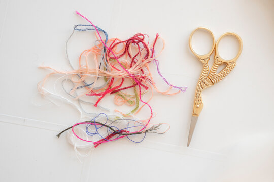 Toma cenital de acercamiento a tijeras de cig&uuml;e&ntilde;a para cortar hilo, junto a mara&ntilde;a de hilos de colores sobre fondo blanco.