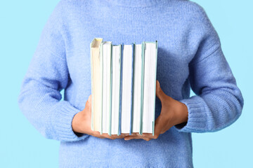 Young woman with stack of books on blue background