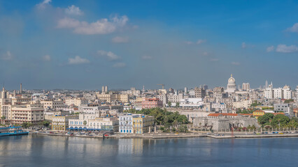 Obraz premium Urban landscape. Multi-storey buildings, old fortress, fort. Cars on the embankment by the bay. The dome of the Capitol on the background of blue sky and clouds. Cuba. Havana.