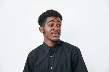 Obraz premium Young black man with dark skin wearing black shirt looking sideways on white background. Portrait of African ethnicity male with natural hair and casual style in studio lighting.