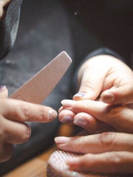 Nail technician filing client's nails at salon