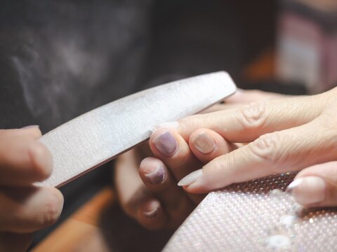 Nail technician filing client's nails