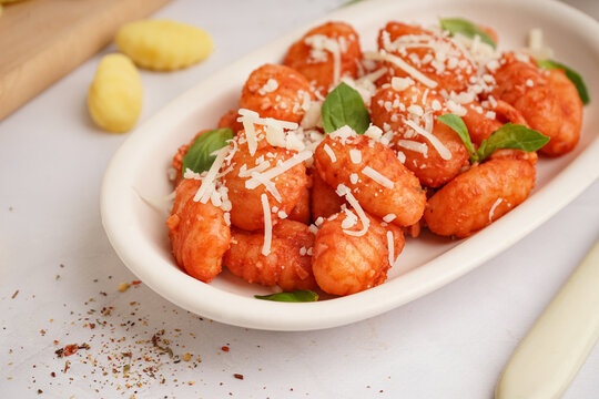 Plate of tasty gnocchi with tomato sauce and cheese on white background