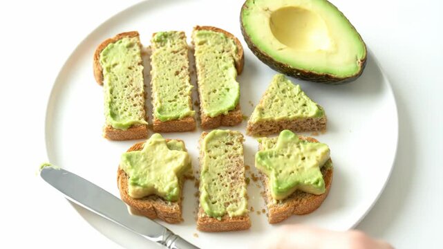 Fresh avocado toast is prepared on a white plate. Various shapes of healthy avocado snacks are ready to eat.