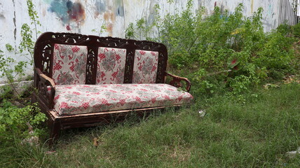 Abandoned couch on grass beside a cracked graffiti wall, highlighting decay, neglect, and nature reclaiming urban spaces.