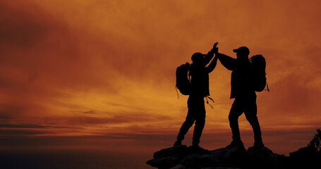 Sunset, silhouette and friends with high five for hike on mountain for vacation, adventure or...