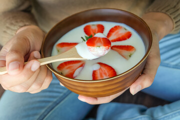Woman holding a bowl of homemade yogurt with fresh strawberry slices, healthy breakfast and clean eating health-boosting foods lifestyle concept