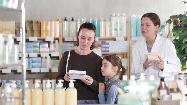 Uncertain mom and daughter making choice of medicine, female druggist helping them in chemist's shop 