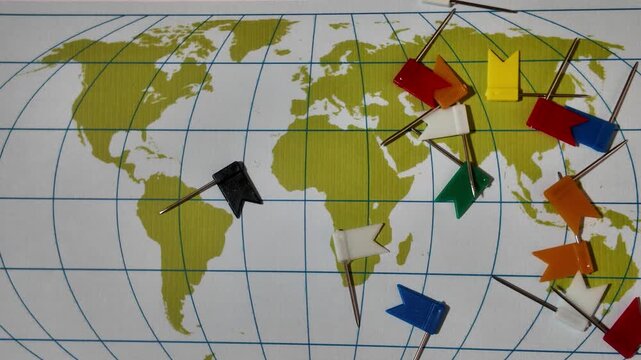 Multicolored plastic flag push pins fall on random marking locations on green continents global map, travel points, or strategic planning