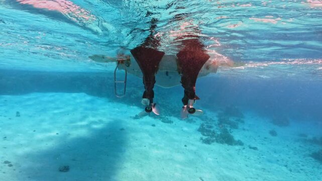 Underwater view of twin outboard motor propellers beneath anchored boat