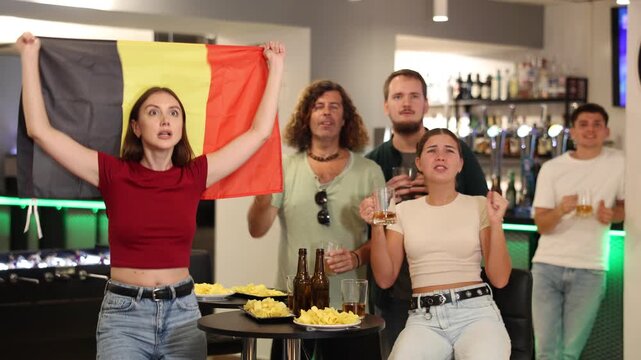 Happy girls adm men with Belgian flag celebrates the victory of her favorite team in a beer bar. High quality 4k footage