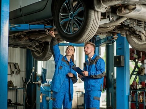 Two automotive technicians inspecting a vehicle on a lift, representing car maintenance, repair services, and mechanical diagnostics.