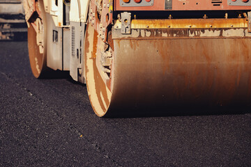 Construction workers utilize powerful equipment to pave a road, applying fresh asphalt while sunlight illuminates the outdoor site. The heavy roller ensures a smooth and durable surface for vehicles.