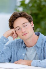 young man with glasses sleeping on the table, tired businessman lying down in the office, closeup of a male worker resting after a long workday
