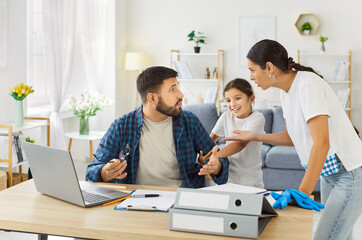 Fototapeta premium Tired father with stress and burnout working at home, mother and child disturb busy dad sitting at desk with laptop and trying to work online. Exhausted man and woman arguing about family chores