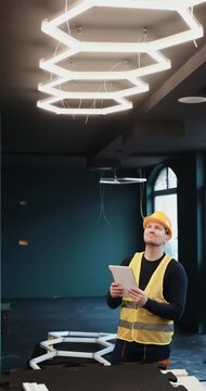 Electrician installing modern hexagon LED ceiling lighting in contemporary interior, using tools and tablet during electrical setup. Professional indoor renovation and smart lighting installation.