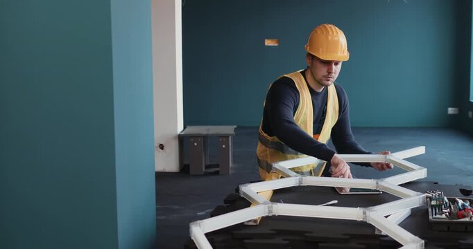 Electrician installing modern hexagon LED ceiling lighting in contemporary interior, using tools and tablet during electrical setup. Professional indoor renovation and smart lighting installation.
