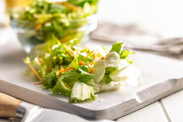 Mix of fresh green salad with carrot on white table.