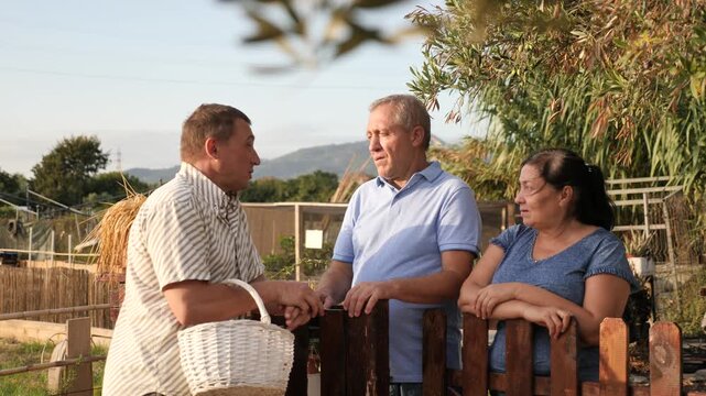 Three neighbours farmers talking together near wooden fence in garden outdoor. High quality 4k footage