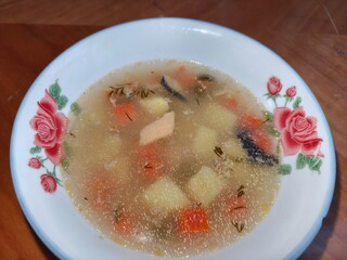 Fish soup with salmon in a white bowl with rose pattern. Comfort food with healthy ingridients. Warm meal for cozy dinner.