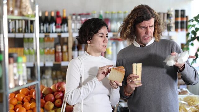 European couple choose natural Swiss cheese in the supermarket. Shoppers look at cheese packages. High quality 4k footage