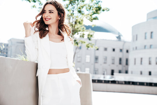 Young beautiful brunette woman wearing nice trendy white suit jacket. Sexy smiling model posing in the street at sunny day. Fashionable female outdoors. Cheerful and happy. Evening makeup, red lips