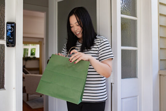Asian woman picking up a package in green paper bag left at the doorstep