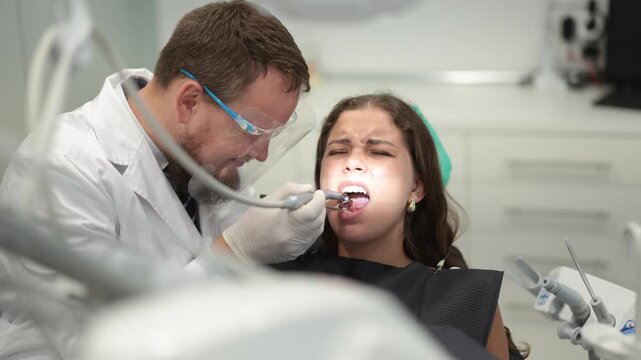 Qualified male dentist carefully drills into a woman tooth to remove caries and make a filling. Woman undergoing treatment in a dental clinic. High quality 4k footage