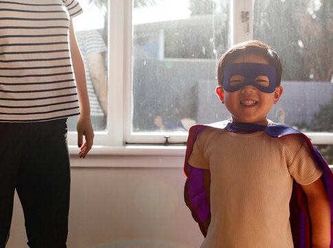 Asian boy wearing superhero costume in the bedroom with mum standing beside him