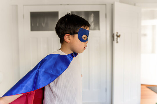 Young Asian boy wearing superhero costume inside home
