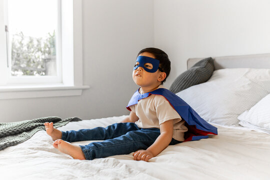 Young Asian boy in superhero costume sitting on the bed