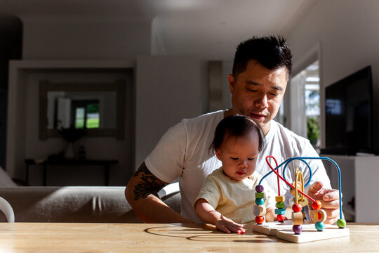 Asian father playing colourful bead maze toy with toddler daughter on the table
