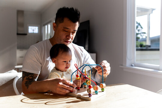 Asian father playing colourful bead maze toy with toddler daughter on the table