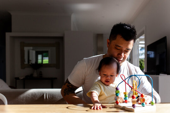 Asian father playing colourful bead maze toy with toddler daughter on the table