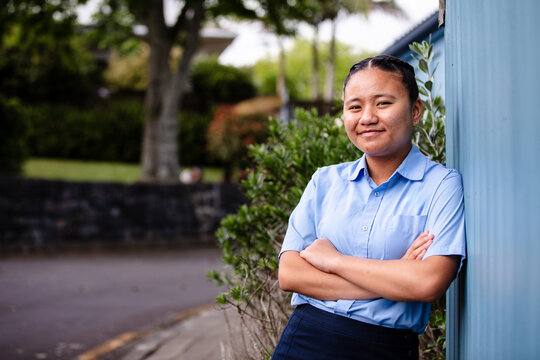 Samoan teenage girl leaning against the blue wall with arms crossed