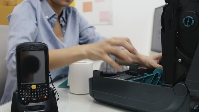 Asian female office workers insert rolls of barcode stickers into the barcode printer.