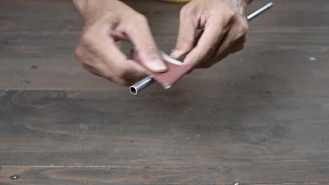 Hands sand an alloy tent frame on a wooden table, making a dry gritty scrape with a sharp hiss