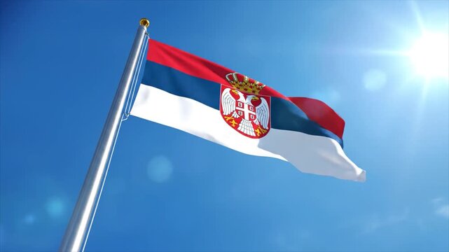 Serbian flag waving on a flagpole against a clear blue sky with sunlight shining brightly from the top right corner