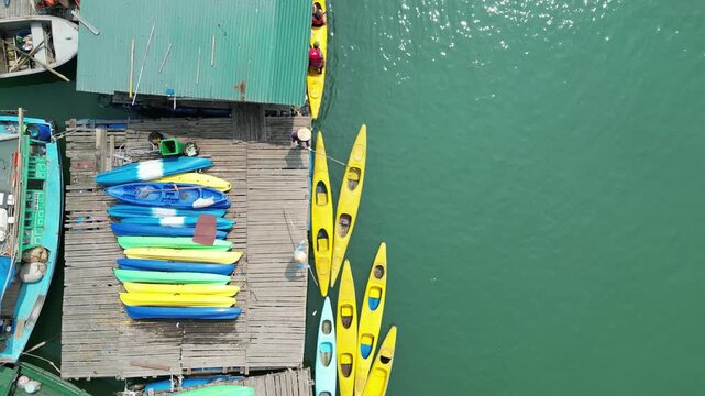 Aerial top view of colorful kayaks on a floating dock in Halong Bay under bright sunlight.