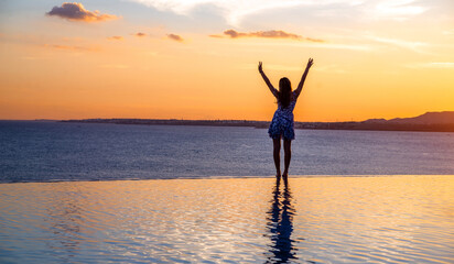 Fototapeta premium A girl stands on the edge of the pool against the background of a sea sunset